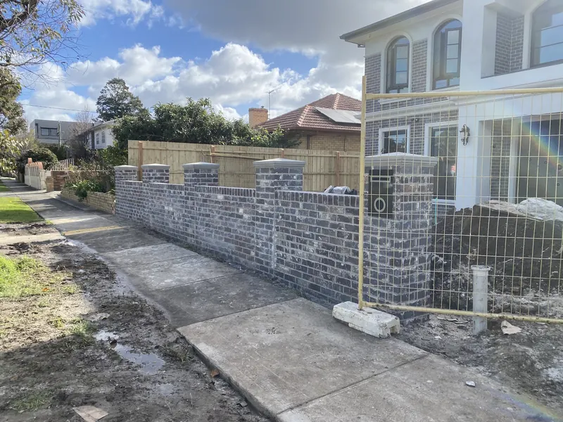 Grey brick front fence with capped piers in front of a double-storey home