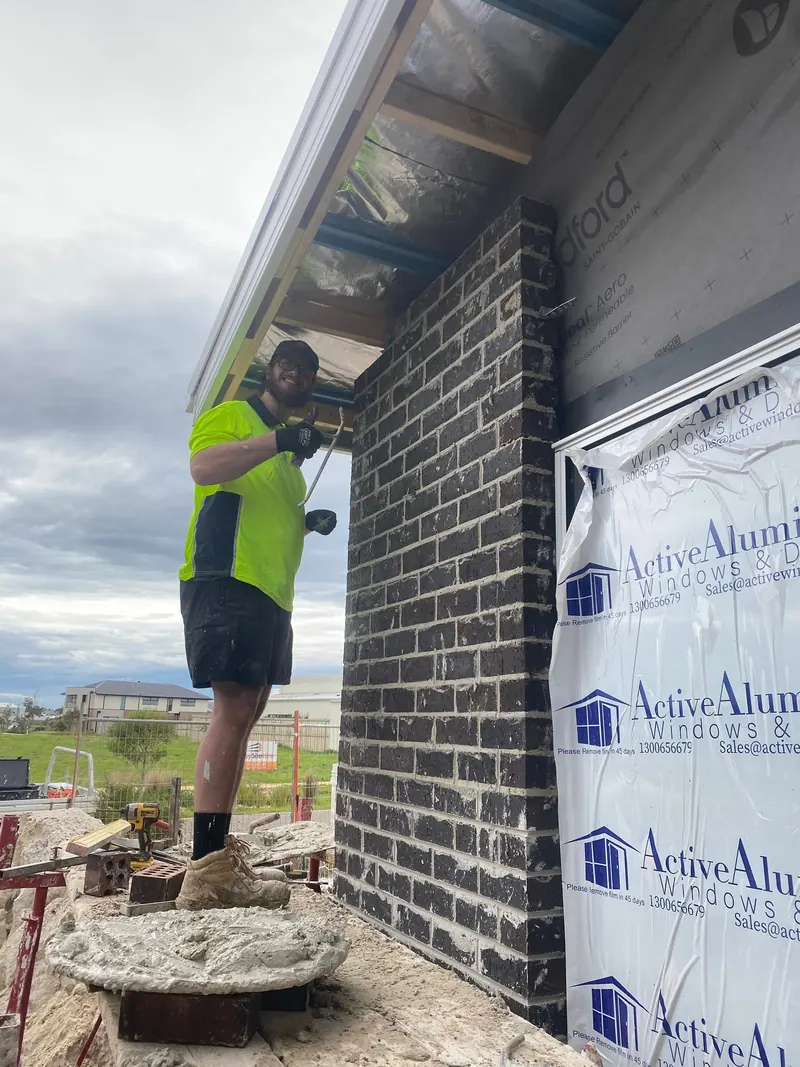Bricklayer laying a dark brick wall under the eave of a new home
